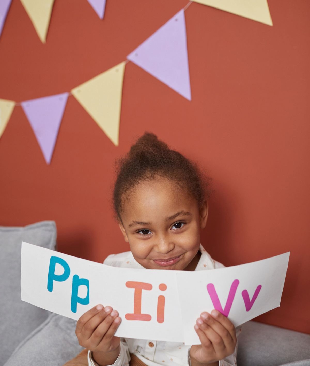 A young girl smiling as she holds up letter cards