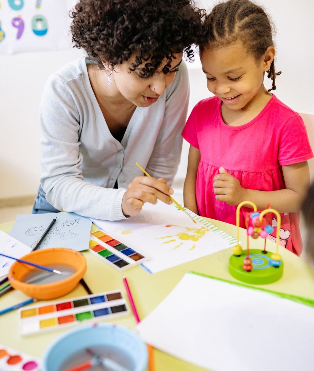An educator and a young girl painting together at a table